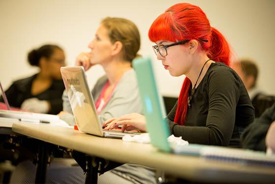 Photo of a Chatham University student with bright red hair working on her laptop in a lecture hall